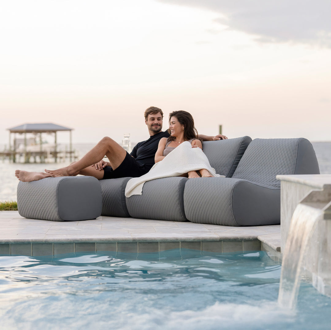 Two people relaxing on a modern outdoor sofa by a poolside. #color_moonlit-gray-outdoor-vegan-leather
