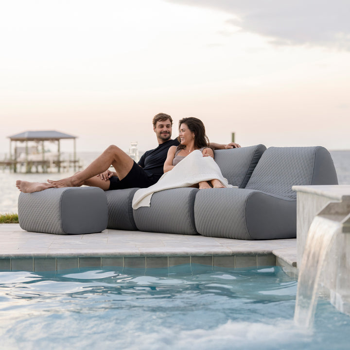 Two people relaxing on a modern outdoor sofa by a poolside. #color_moonlit-gray-outdoor-vegan-leather