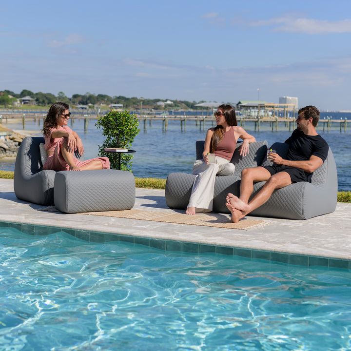 Three people sitting on modern outdoor furniture by a pool with a scenic background. #color_moonlit-gray-outdoor-vegan-leather