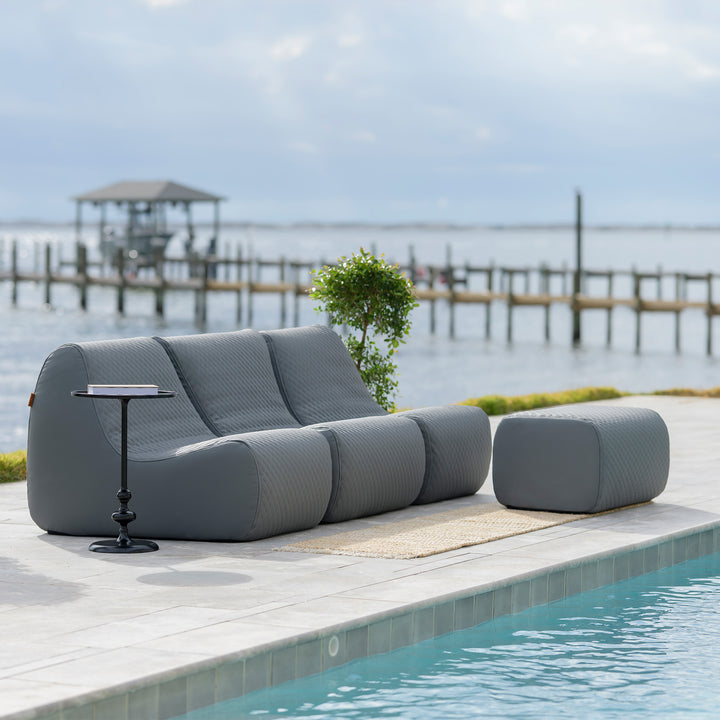 Gray outdoor sofa with a small table by a pool with a dock and water in the background #color_moonlit-gray-outdoor-vegan-leather