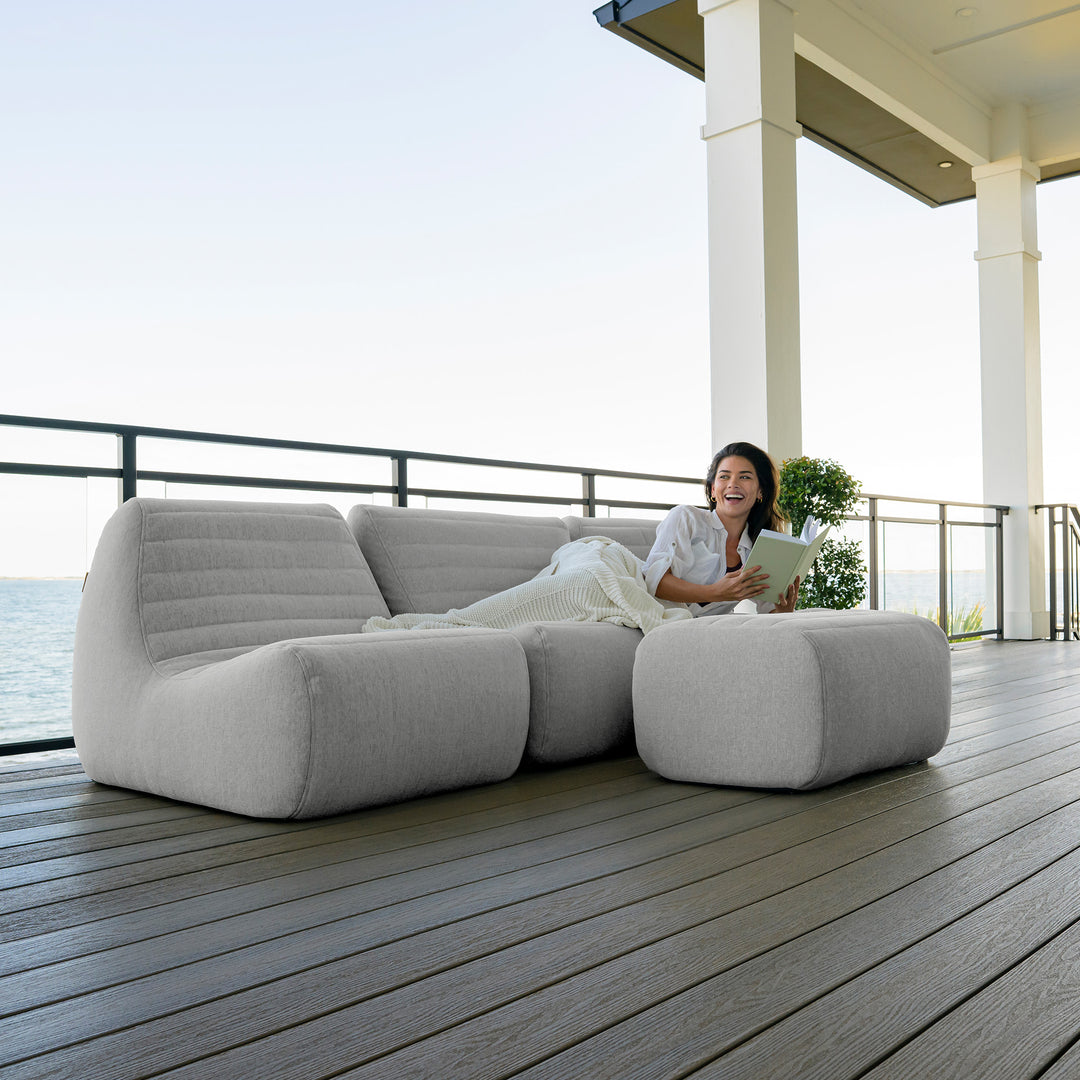 Woman lying on a modern outdoor sofa by the sea #color_port-gray-outdoor-performance-linen