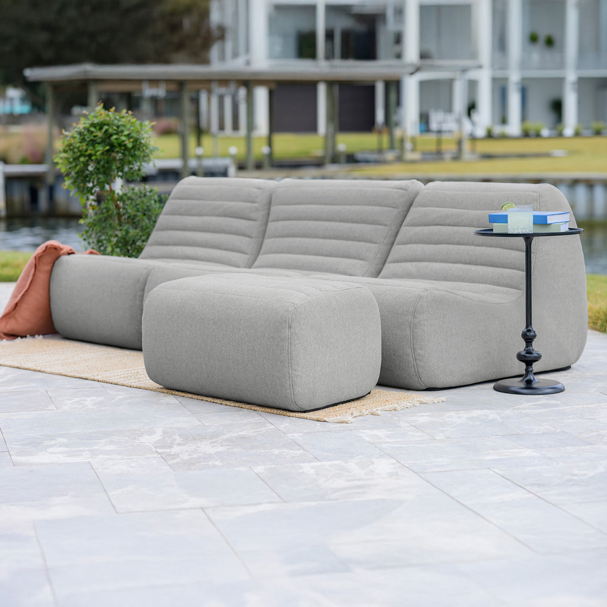 Gray outdoor sofa with a small table on a patio near a body of water. 