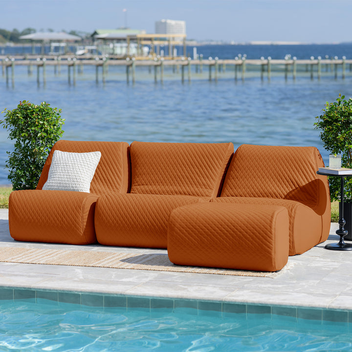 Orange sectional sofa with a white pillow on a patio by a pool with a scenic background. #color_honey-sand-outdoor-vegan-leather