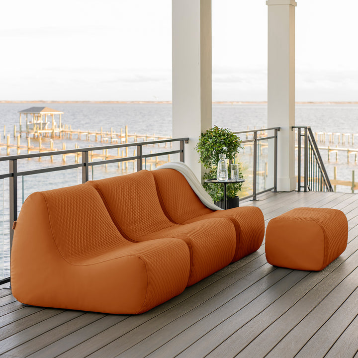 Orange outdoor sofa and ottoman on a deck with water view #color_honey-sand-outdoor-vegan-leather