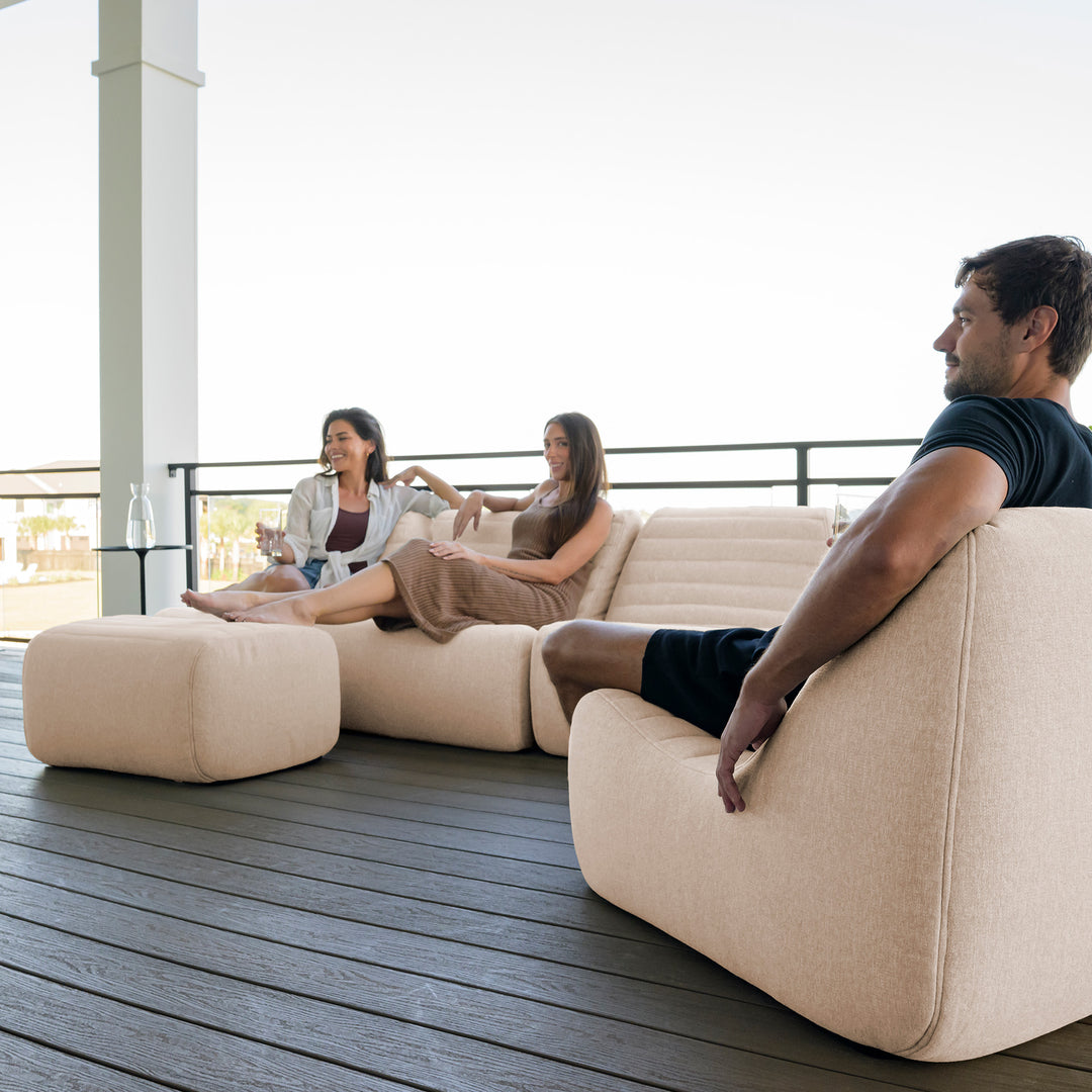 People sitting on a modern beige outdoor sofa with a view of a building in the background. #color_sunlit-cream-outdoor-performance-linen
