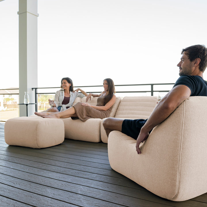 People sitting on a modern beige outdoor sofa with a view of a building in the background. #color_sunlit-cream-outdoor-performance-linen