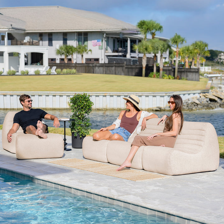 People sitting on a sofa by a pool with a house and trees in the background #color_sunlit-cream-outdoor-performance-linen
