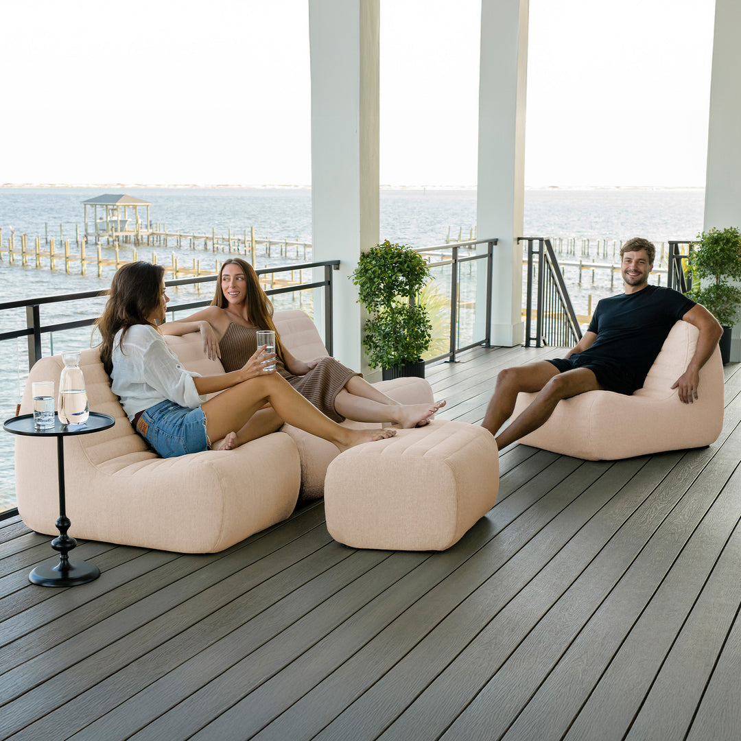 Three people relaxing on beige bean bags on a wooden deck with ocean view #color_sunlit-cream-outdoor-performance-linen