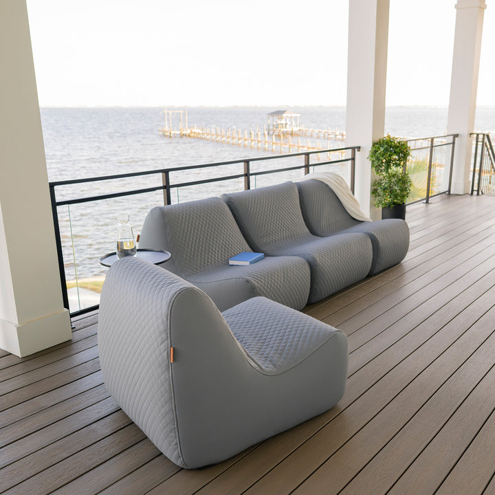Gray outdoor sofa on a wooden deck with a waterfront view #color_moonlit-gray-outdoor-vegan-leather