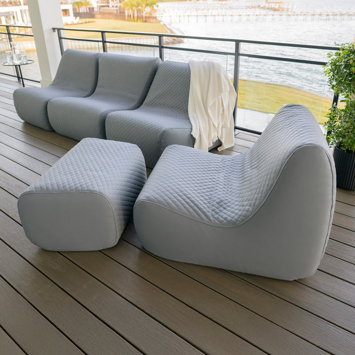 Modern outdoor furniture set on a wooden deck with a view of water and greenery. #color_moonlit-gray-outdoor-vegan-leather