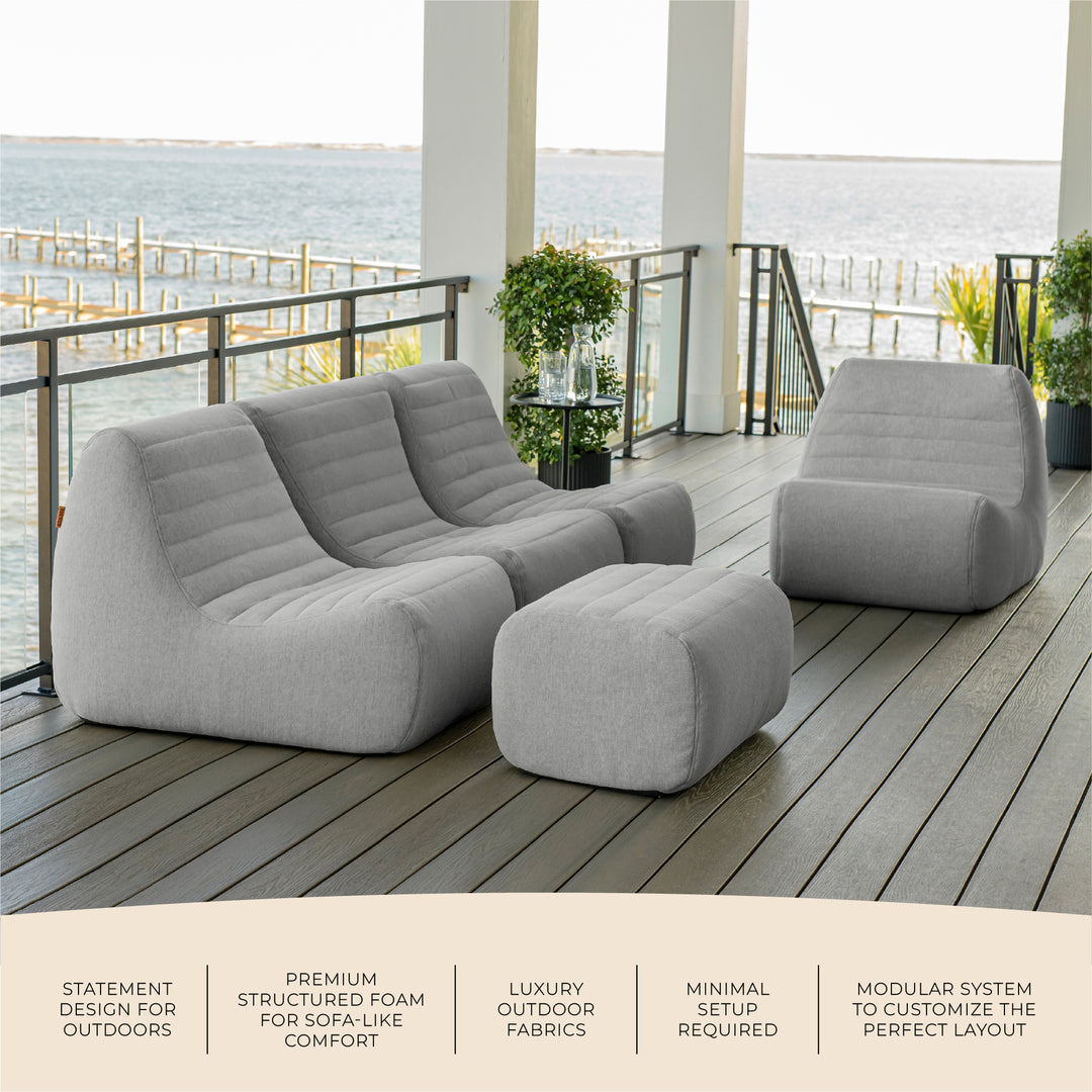 Gray outdoor sofa and ottoman set on a deck with ocean view. #color_port-gray-outdoor-performance-linen
