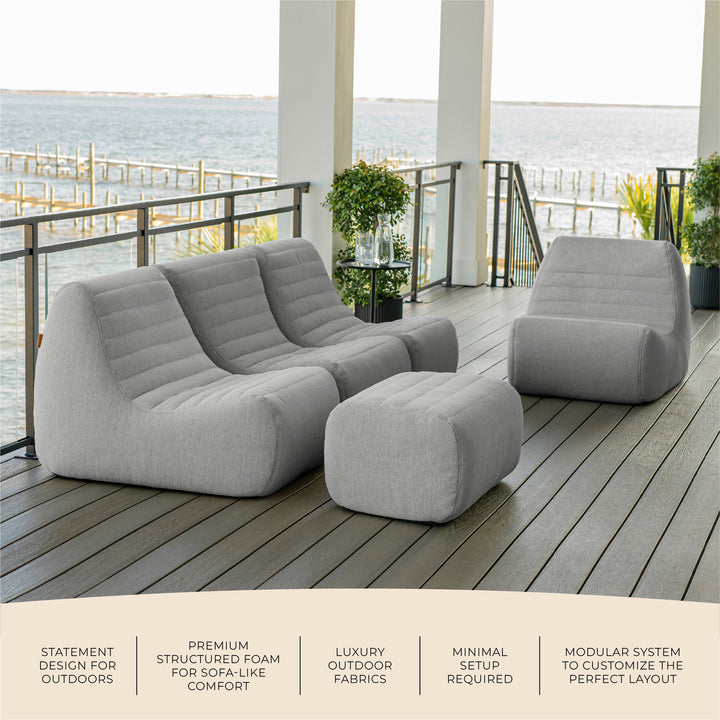 Gray outdoor sofa and ottoman set on a deck with ocean view. #color_port-gray-outdoor-performance-linen