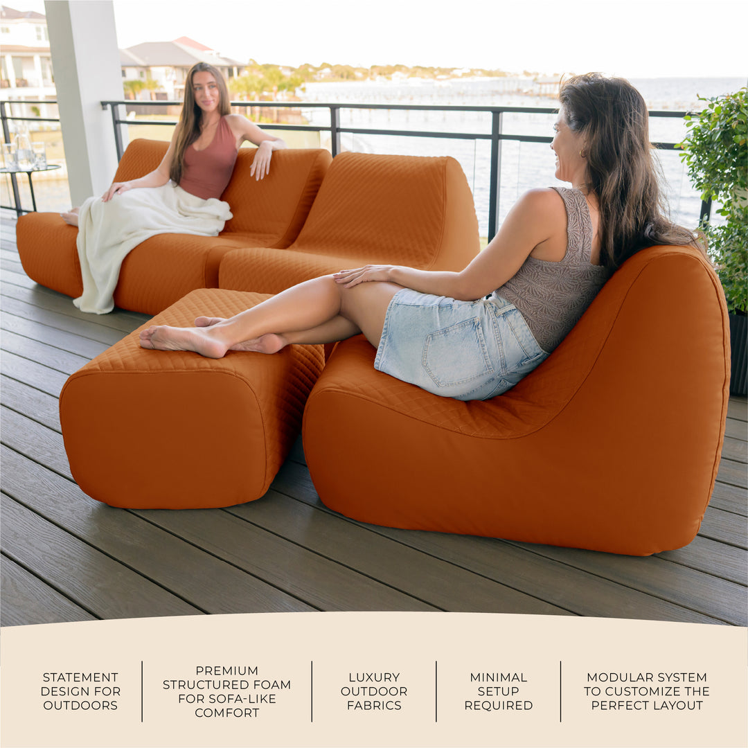 Two women sitting on an orange outdoor sofa on a wooden deck. #color_honey-sand-outdoor-vegan-leather