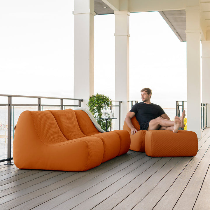 Orange outdoor sofa set on a wooden deck with a person sitting on one of the cushions. #color_honey-sand-outdoor-vegan-leather