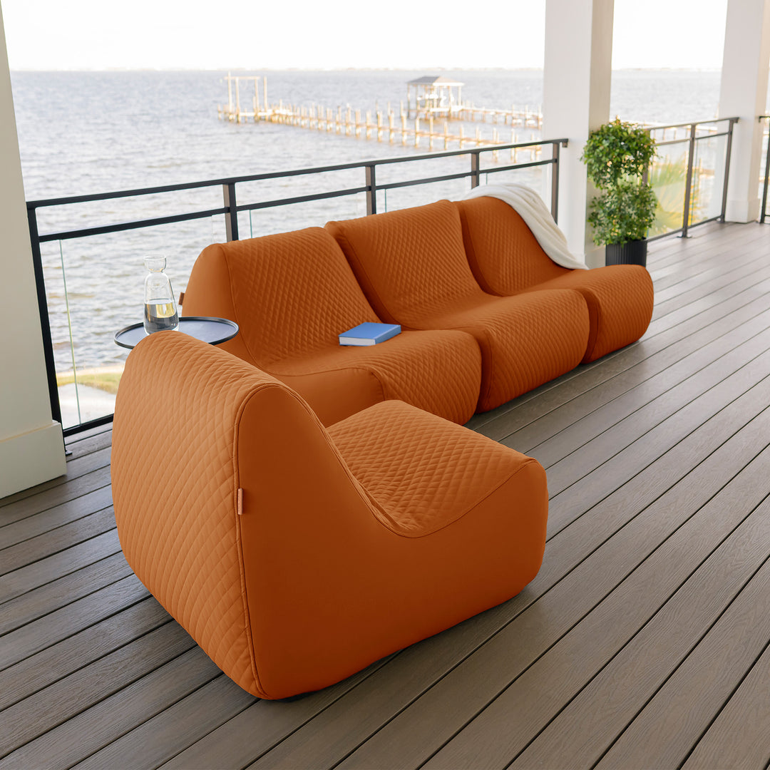 Orange outdoor sofa on a wooden deck with a waterfront view. #color_honey-sand-outdoor-vegan-leather
