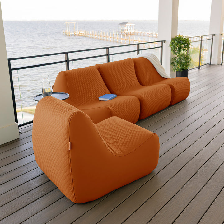 Orange outdoor sofa on a wooden deck with a waterfront view. #color_honey-sand-outdoor-vegan-leather