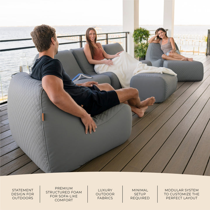 People relaxing on a modern outdoor sofa set with a view of water. #color_moonlit-gray-outdoor-vegan-leather