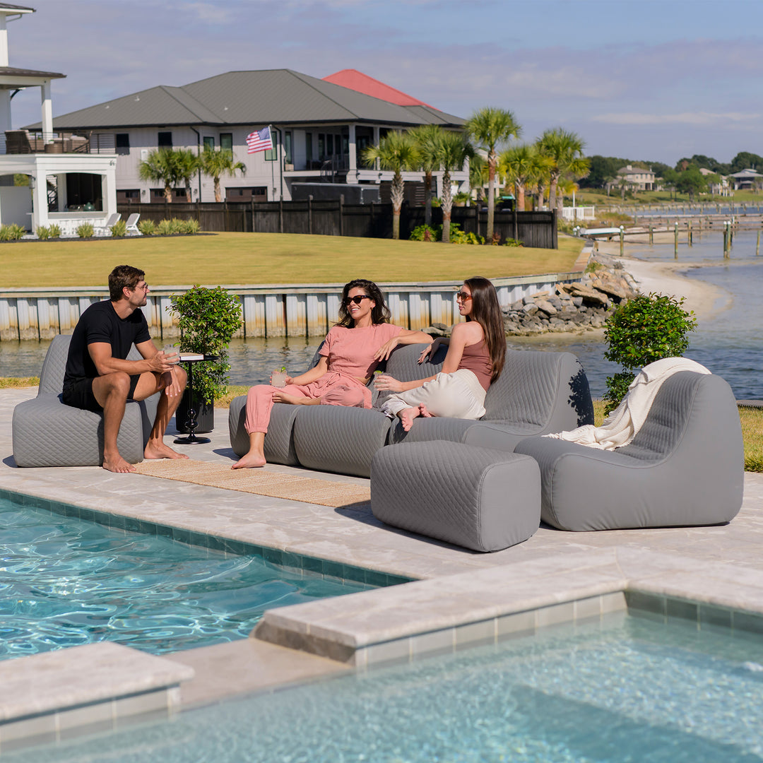 People sitting on inflatable lounge chairs by a pool with a waterfront view. #color_moonlit-gray-outdoor-vegan-leather