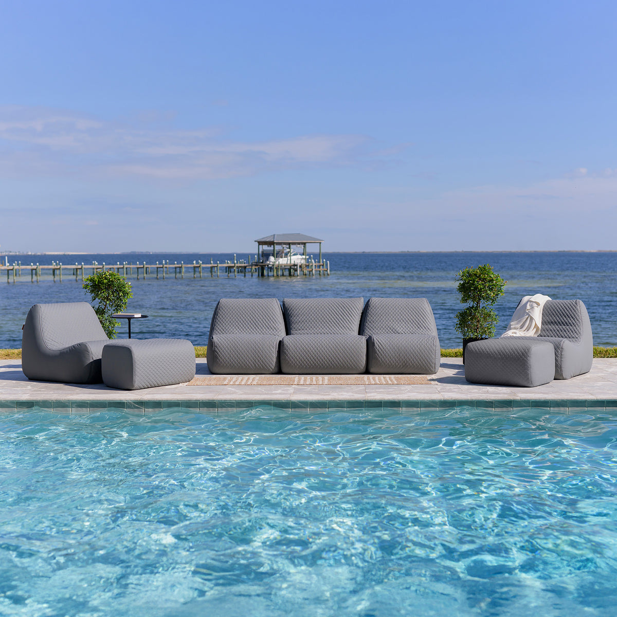Gray outdoor sofa set by a pool with a scenic background of water and sky. 
