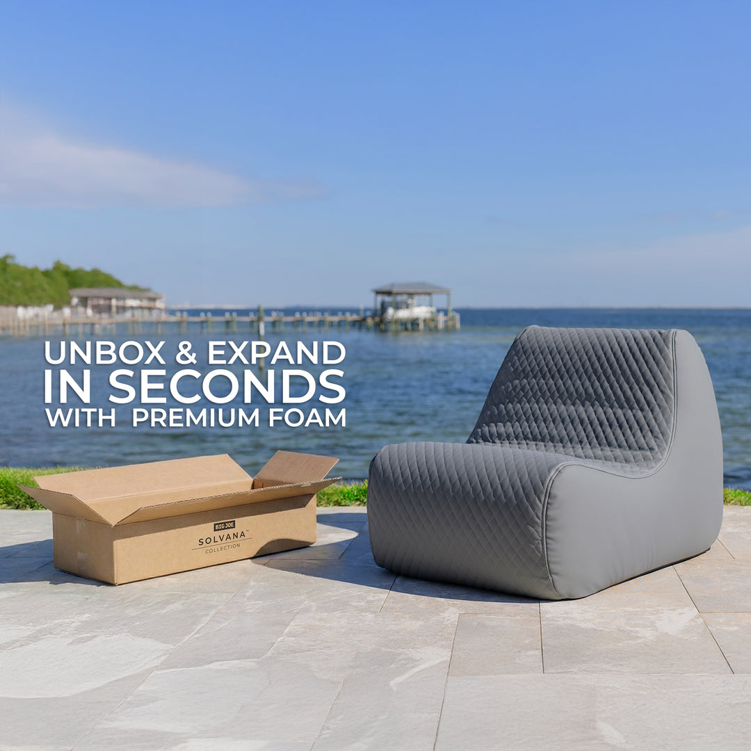 Gray sectional chair next to an open box with a scenic background of water and sky. #color_moonlit-gray-outdoor-vegan-leather