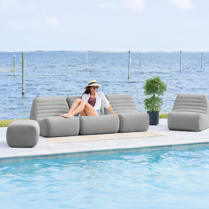 Woman sitting on an inflatable outdoor sofa by a pool with a scenic background #color_port-gray-outdoor-performance-linen