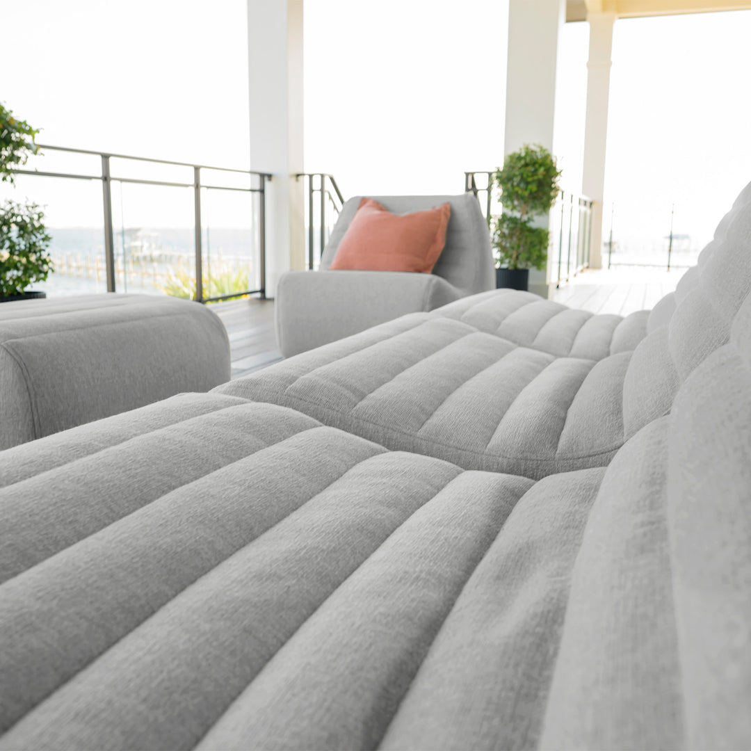 Gray sectional sofa with a pink pillow in a modern living room. #color_port-gray-outdoor-performance-linen