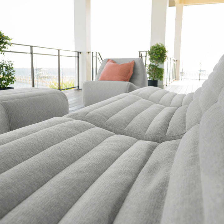 Gray sectional sofa with a pink pillow in a modern living room. #color_port-gray-outdoor-performance-linen