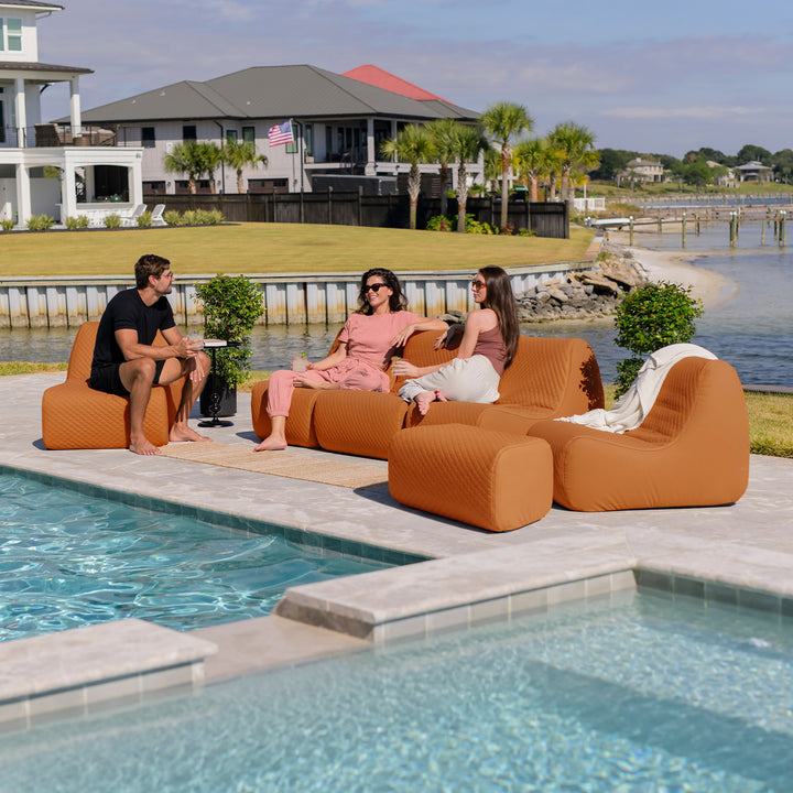 People relaxing on orange outdoor furniture by a pool with a waterfront view. #color_honey-sand-outdoor-vegan-leather
