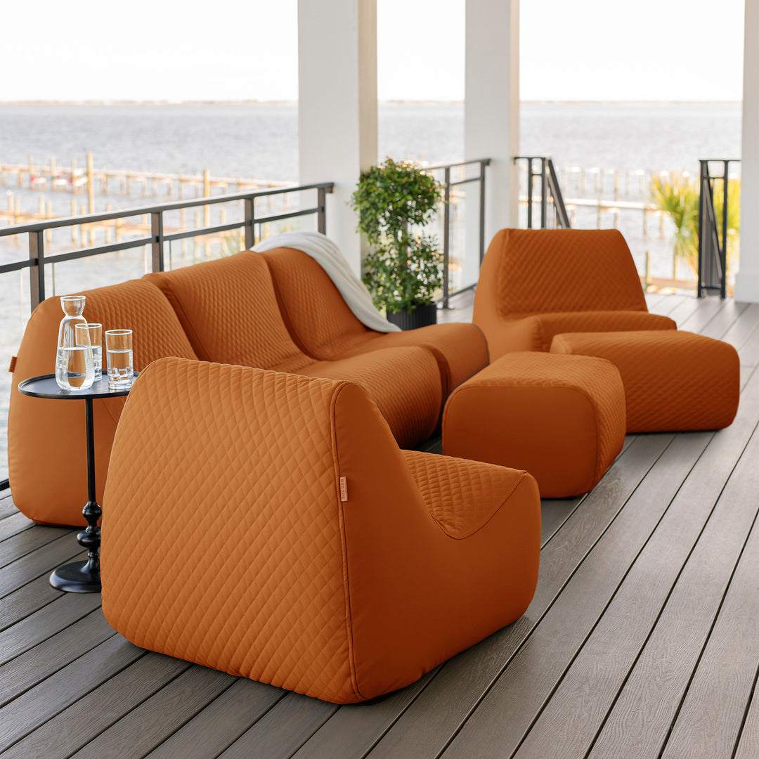 Orange outdoor furniture set on a wooden deck with a view of water. #color_honey-sand-outdoor-vegan-leather