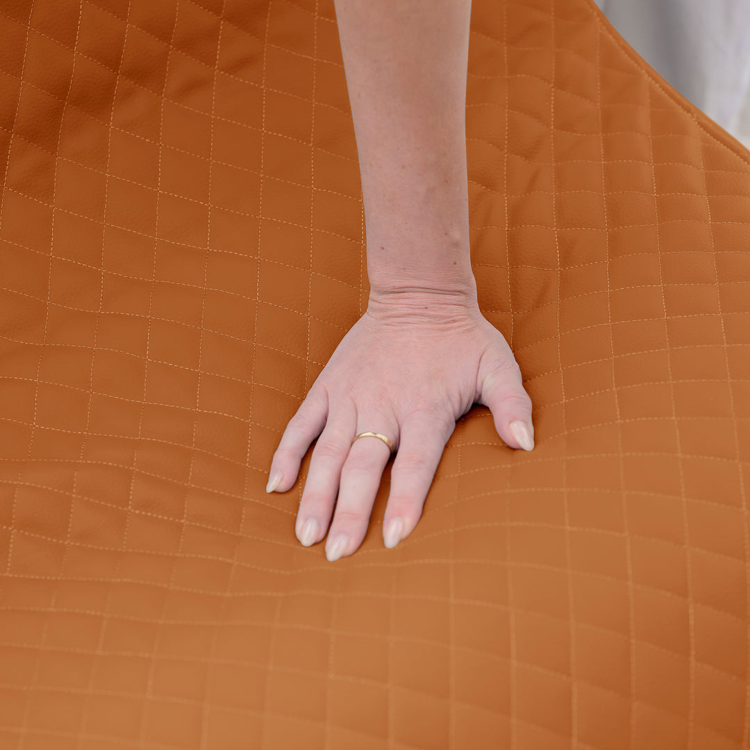 Hand on a brown quilted surface #color_honey-sand-outdoor-vegan-leather