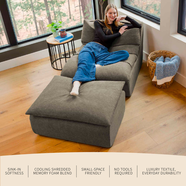 Person lounging on a gray sectional sofa in a room with large windows. 