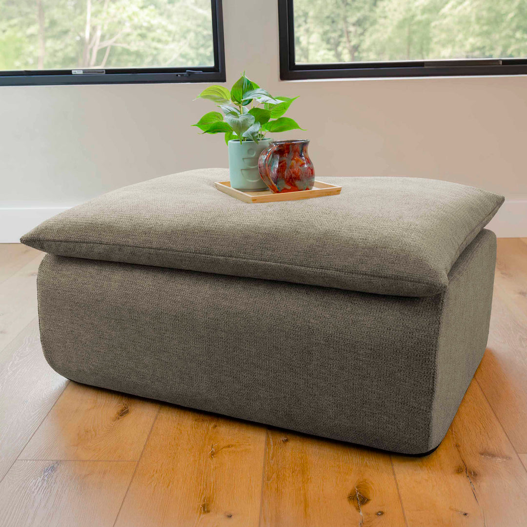 Gray ottoman with a plant and mug on a wooden floor 