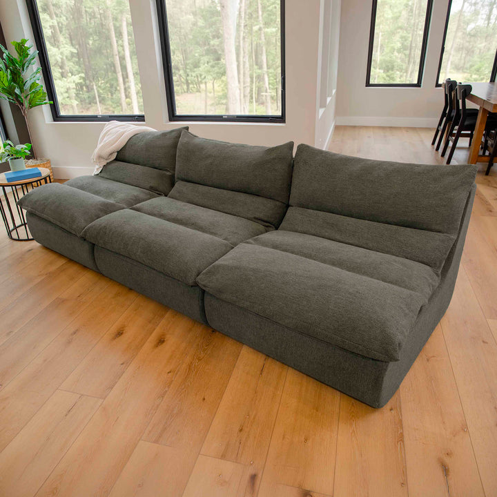 Green sectional sofa in a room with large windows and wooden flooring 