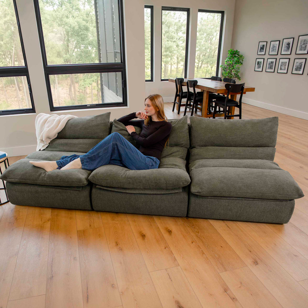 Woman sitting on a large olive green sectional sofa in a modern living room. 