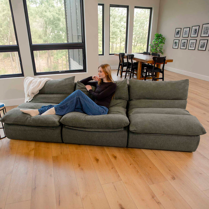 Woman sitting on a large olive green sectional sofa in a modern living room. 