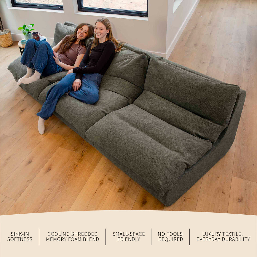 Two people sitting on a olive green sectional sofa in a room with wooden flooring. 