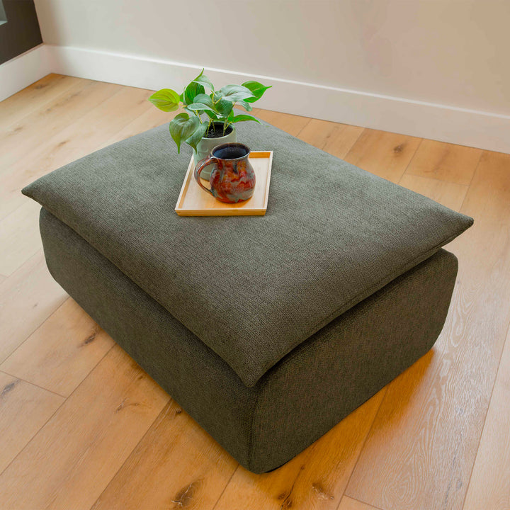 Green ottoman with a plant and mug on a wooden floor 