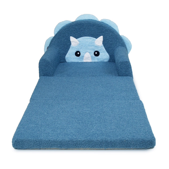 A blue plush pet bed shaped like a dinosaur, featuring a soft blue body, a backrest with cloud-like edges, and a cute light blue dinosaur face with white horns and black eyes. 