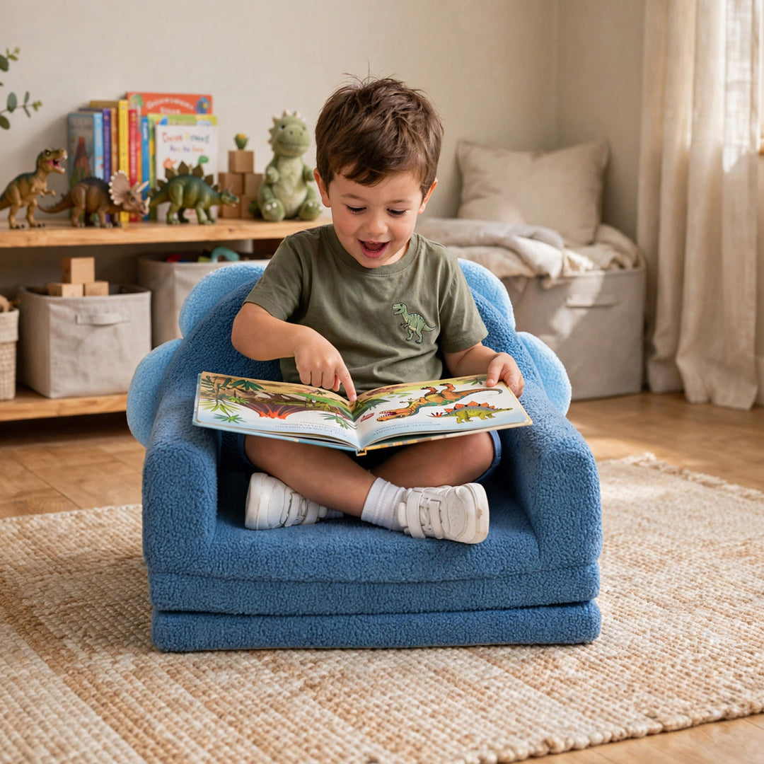 A young child sitting cross-legged in a small blue plush armchair, reading a colorful children&