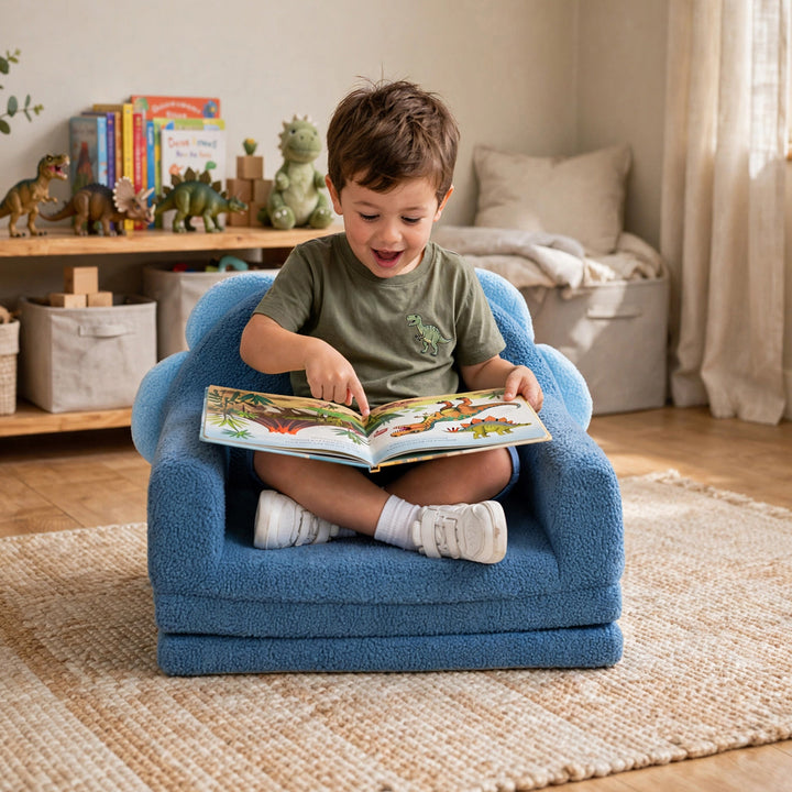 A young child sitting cross-legged in a small blue plush armchair, reading a colorful children&