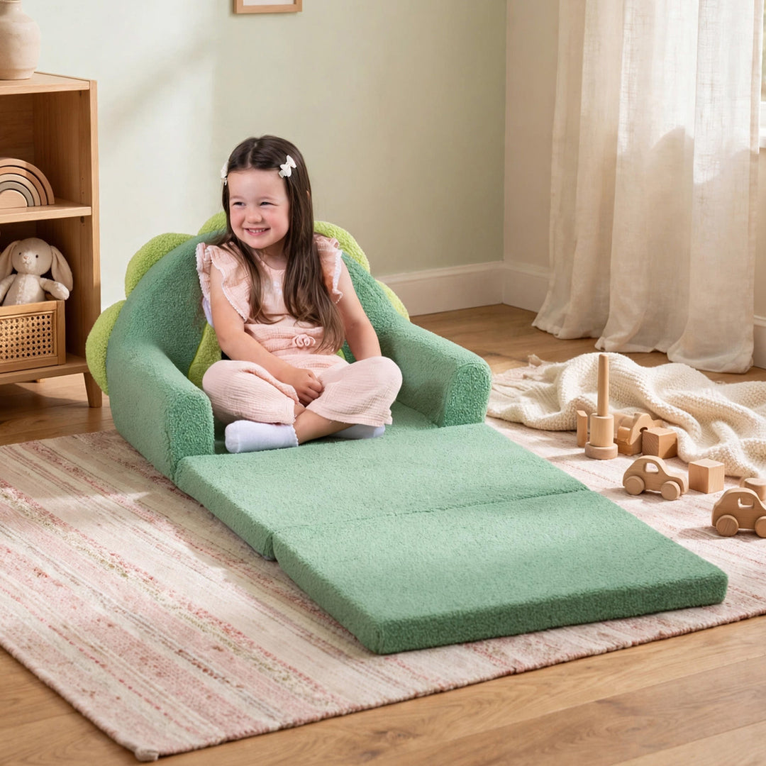 A young girl sits smiling on a green plush armchair-style floor cushion with an attached rectangular foam pad, set in a child&