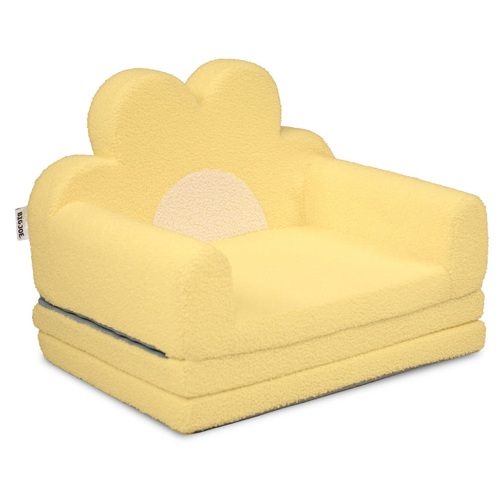 A yellow plush armchair designed like a flower, featuring a textured bouclé fabric, a matching flower-shaped backrest, and a semi-circular sun motif on the back, shown on a plain white background. 