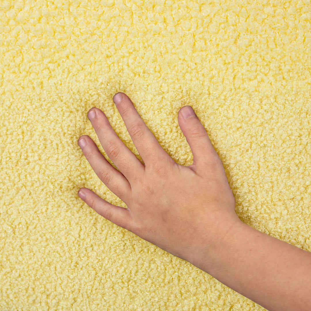 A close-up of a hand pressing down on a textured, fluffy yellow surface to demonstrate its softness and tactile quality. 