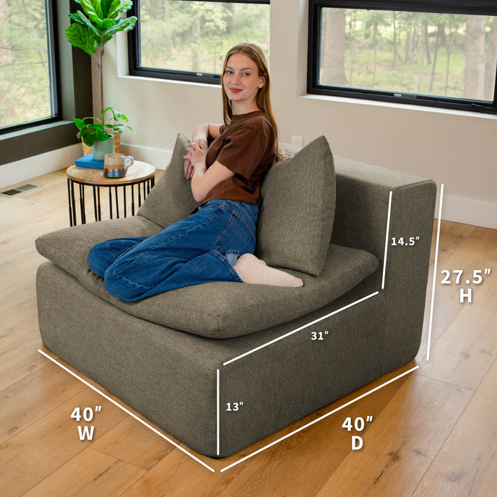 Woman sitting on a gray sofa with dimensions labeled in a room with large windows. 