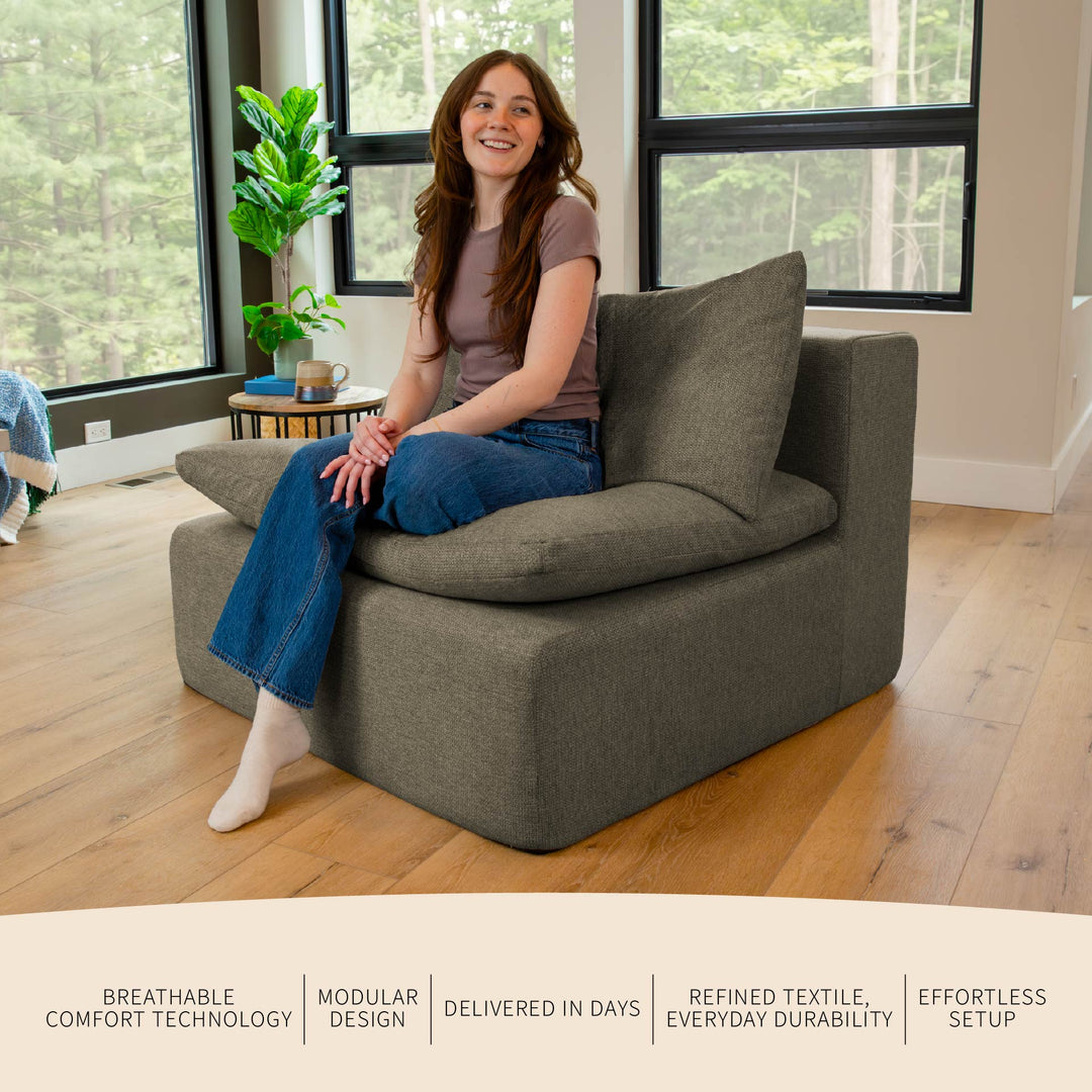 Woman sitting on a gray sofa in a bright room with large windows. 