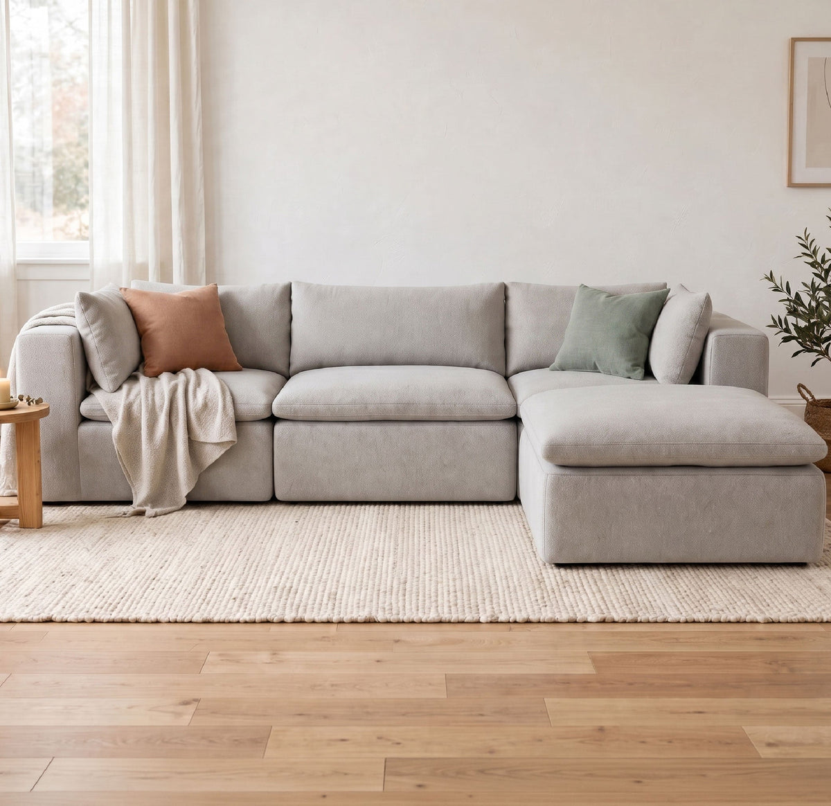 A light gray modular sectional sofa with a chaise lounge, styled in a bright, modern living room with light wood floors, a beige rug, and neutral accent pillows.