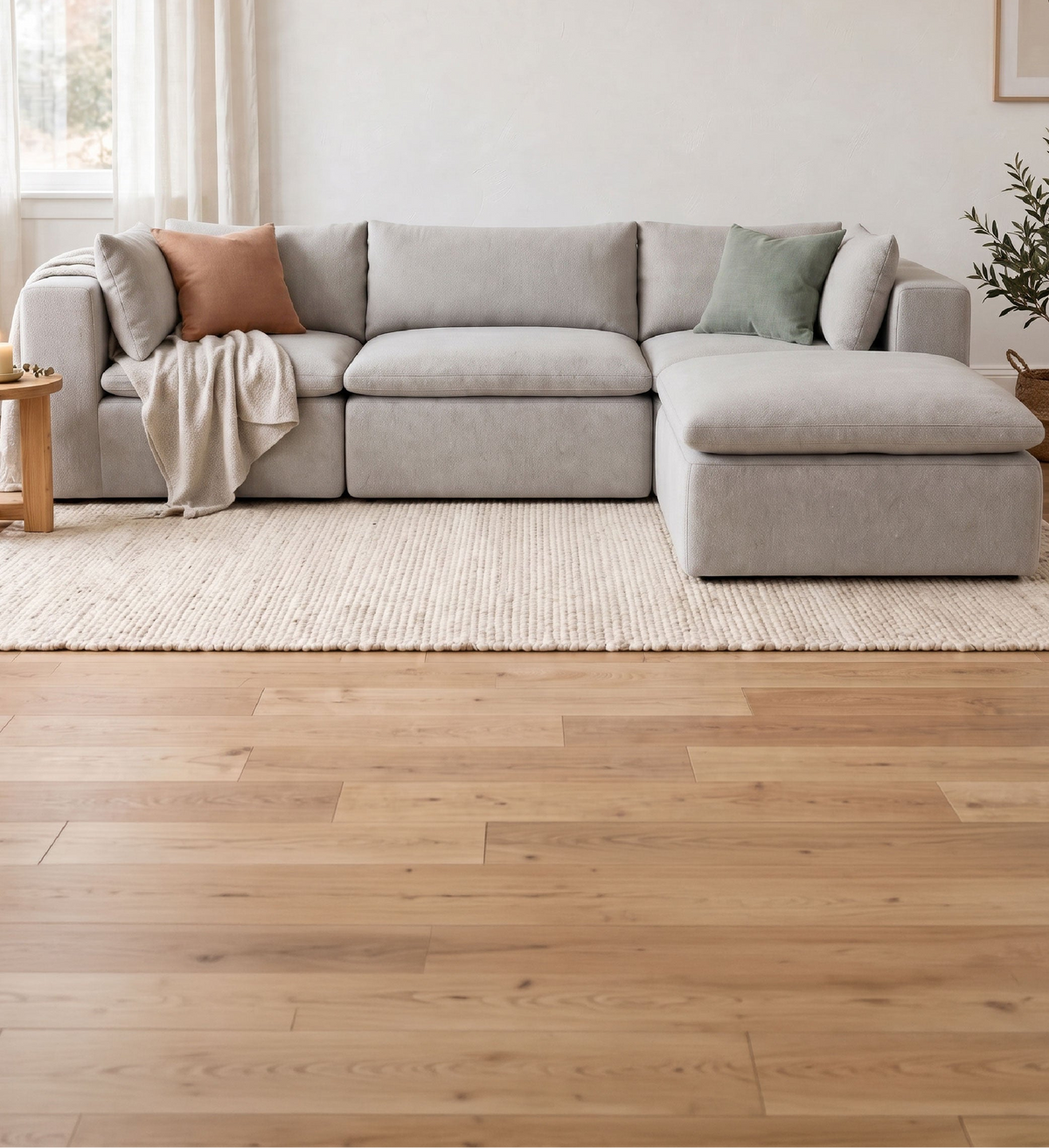 A light gray modular sectional sofa with a chaise lounge, styled in a bright, modern living room with light wood floors, a beige rug, and neutral accent pillows.