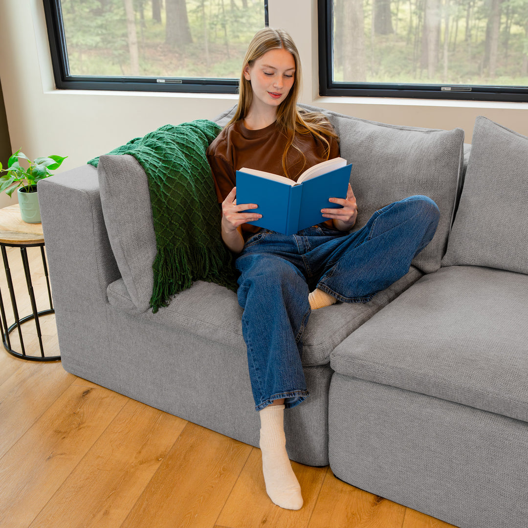 Woman reading a book on a gray corner sectional piece in a living room 