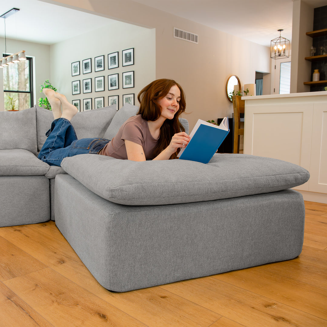 Woman lounging on the ottoman part of a sectional couch reading a book 