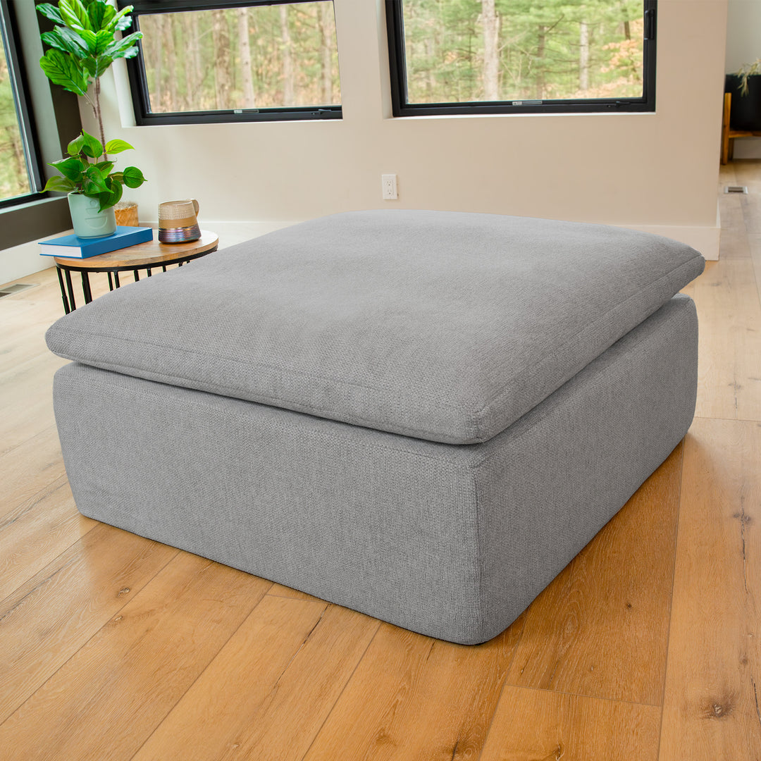 Gray ottoman in a room with wooden floor and large windows 
